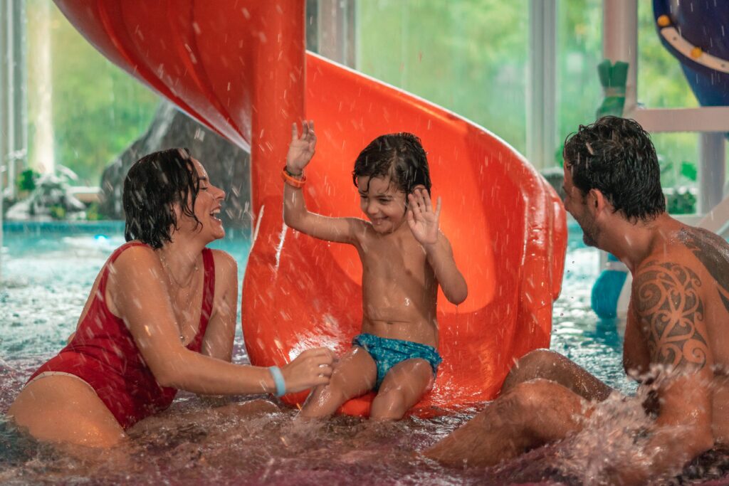 Família brincando em uma piscina enquanto o filho está sentado em um toboágua laranja. Família brincando em uma piscina enquanto o filho está sentado em um toboágua laranja.